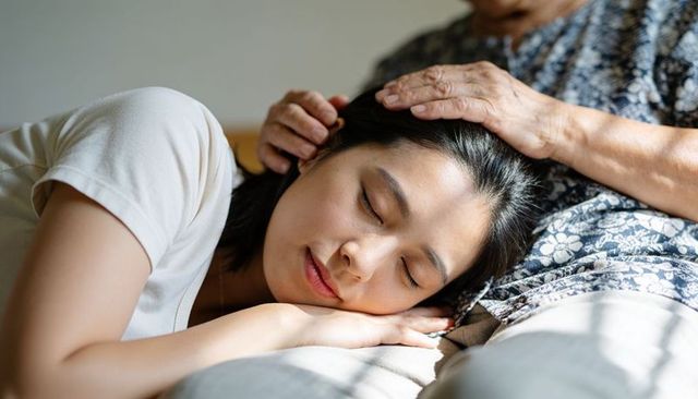 Young woman resting head on elder's lap receiving gentle care and comforting touch at home