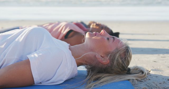Women lying on yoga mats at sandy beach, appearing relaxed and peaceful. Ideal for use in promoting wellness retreats, yoga classes, meditation practices, beach activities, and healthy lifestyles.