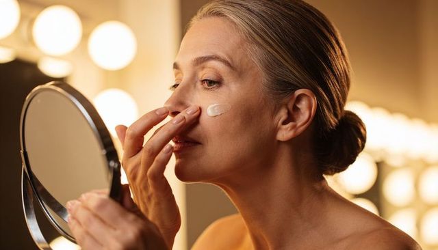 Mature woman applying face cream at vanity mirror for skincare and anti-aging routine