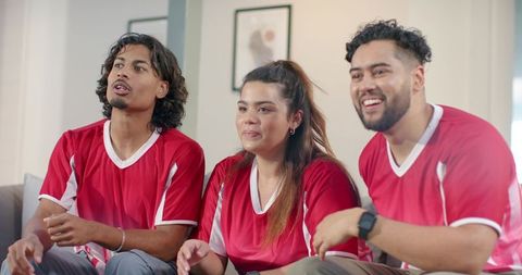 Friends watching live sports at home wearing matching red jerseys and cheering