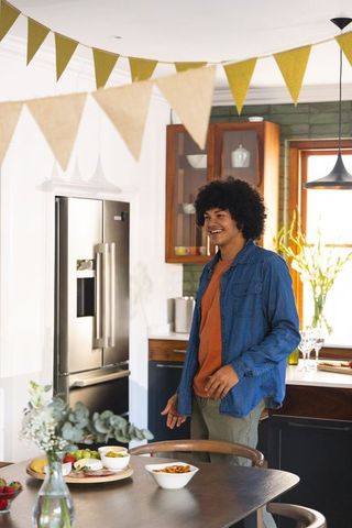 African american man 20s standing at dining table smiling and gesturing in kitchen gathering