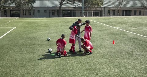 Coach instructing young soccer players in dribbling skills on field