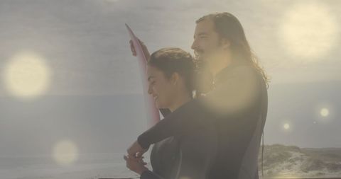 Couple Holding Surfboard at Beach with Bright Lens Flares