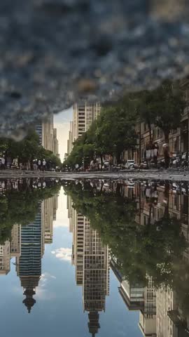 Vertical Puddle Reflection Capturing Symmetric City Avenue Skyline and Commuters Walking