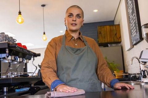Confident barista cleaning counter in modern cafe wearing green apron and brown shirt