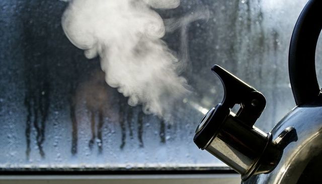 Steaming whistling kettle releasing plume at fogged window sill, cozy kitchen moment