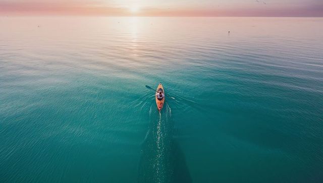Solitary Kayaker Paddling Toward Sunrise on Tranquil Blue Sea