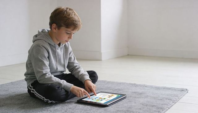 Young boy using tablet on gray rug in sunlit minimal room for learning and playtime