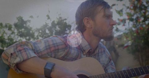 Man Playing Guitar in Sunlit Outdoors with Rustic Feel