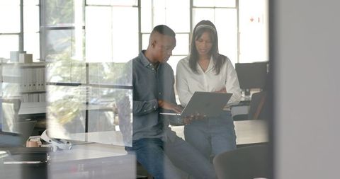 Colleagues collaborating on project using laptop in modern office