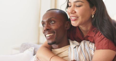 Smiling couple sharing hug on sunlit sofa, cozy at-home embrace and romantic moment