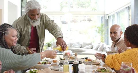 Multigenerational diverse family sharing sunny brunch around wooden table in modern home
