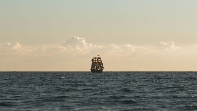 Majestic three-masted ship sailing on open ocean at sunset