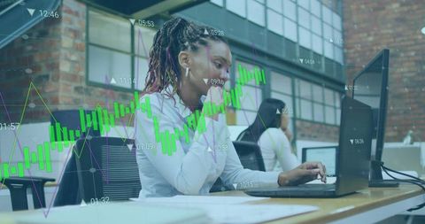 Businesswoman analyzing financial candlestick charts on laptop in modern open-plan office