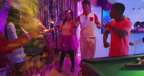 Young adults holding sparklers celebrating birthday party by pool table with neon lights