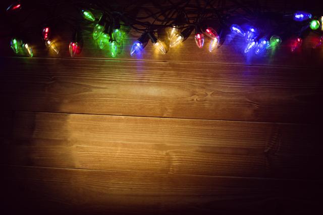 Colorful Christmas lights glowing on a wooden background creating a festive atmosphere. Suitable for holiday greeting cards, Christmas-themed social media posts, or festive website banners.