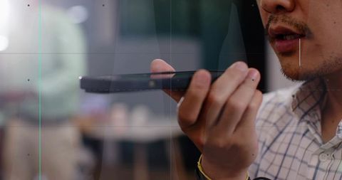 Mid-adult Asian man holding smartphone and speaking into device in coworking office environment