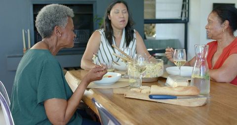 Multigenerational diverse women sharing meal around wooden table laughing and talking