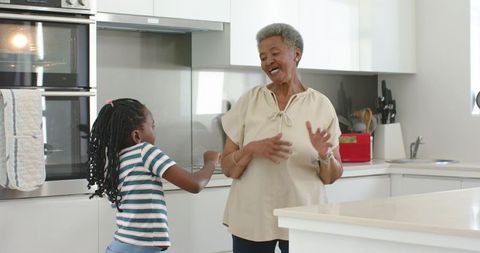 African american grandmother and granddaughter dancing joyfully in bright modern kitchen