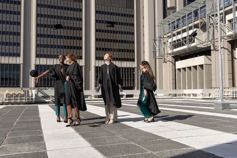 Diverse female graduates celebrating on rooftop terrace tossing caps while holding diplomas