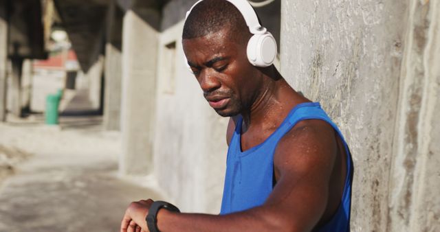 African american man wearing headphones checking his smartphone, exercising outdoors on sunny day. fitness, healthy and active lifestyle concept.
