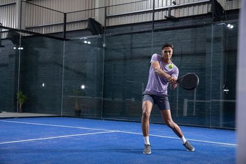 African american athlete hitting neon padel ball with black racket on indoor blue court