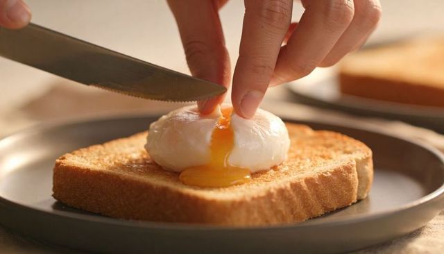 Poached egg breaking on golden toast closeup with runny yolk and knife action