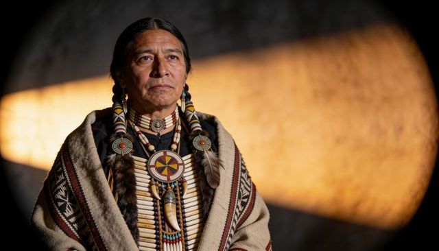 Native american elder wearing beaded breastplate, feather adornments and woven robe portrait