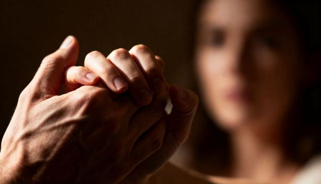 Hands clasping in tender support between partners with warm moody lighting and close-up
