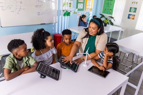 Students exploring renewable energy with teacher using solar panels and wind turbine