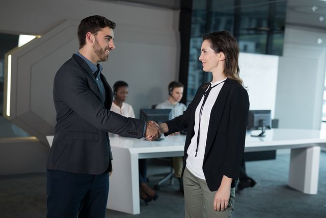 Business professionals shaking hands in a modern office setting, symbolizing agreement and successful collaboration. Ideal for use in business-related content, corporate websites, teamwork and partnership promotions, and professional training materials.