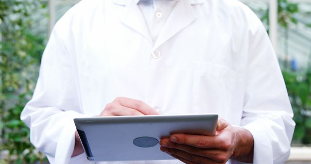 Scientist in white lab coat using tablet outdoors. Image suggests modern technology usage in scientific research or healthcare. Useful for topics on biomedical research, biotechnology, data analysis, digital healthcare solutions, and scientific innovation.
