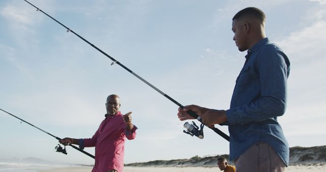 Father and son standing on a sandy beach, fishing together with rods. Ideal for use in family bonding, leisure activities, outdoor pursuits, summer adventures, and father-son relationship-related content.
