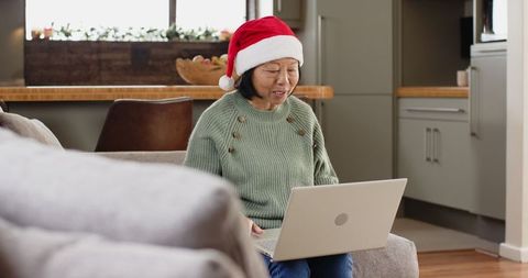 Senior Asian Woman Wearing Santa Hat Using Laptop at Home