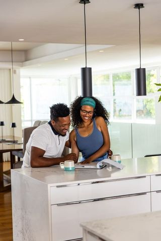 Diverse couple leaning over marble kitchen island reviewing documents and smiling