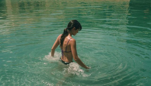 Wading woman in green lagoon creating ripples wearing purple bikini top and dark bottoms