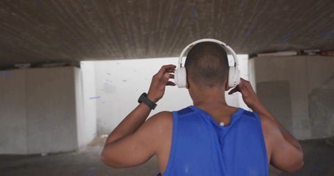 Adjusting headphones under urban underpass — runner with fitness tracker and blue tank