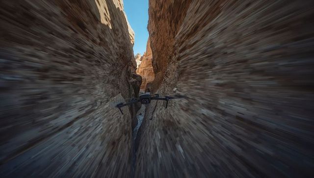 Drone flying through narrow slot canyon at high speed with motion blur and sandstone walls