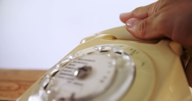 A person's hand is seen dialing on a vintage rotary telephone, with copy space. Capturing a moment of communication, the image evokes a sense of nostalgia for past technology.