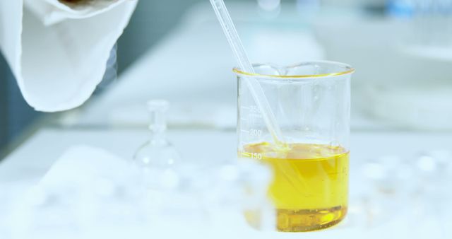 Scientist conducting an experiment with a yellow liquid in a glass beaker using a pipette. Ideal for use in promotions for scientific research, laboratory equipment, chemistry studies, and educational materials.
