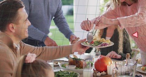Family passing plate and serving autumn meal on porch table with pumpkin and candles