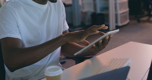 Male working with digital tablet at desk in contemporary office environment. This image highlights casual work setting, making it ideal for use in articles about remote work, technology in office environments, and productivity tips.