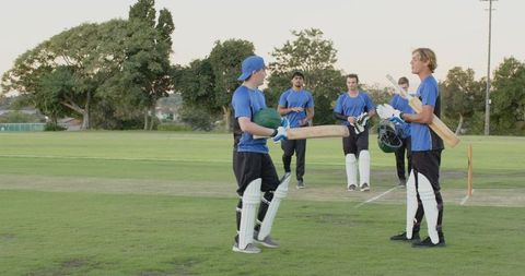 Cricket teammates walking across pitch holding bats and helmets before match