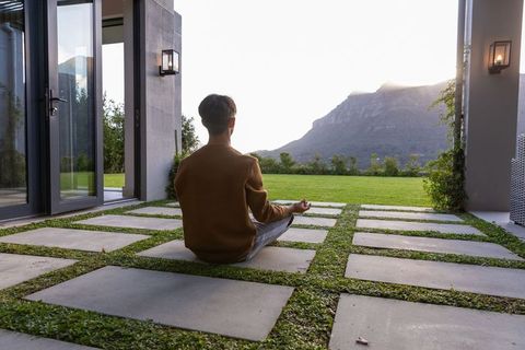 Meditating person on modern patio with grass-grid pavers and mountain view at sunrise