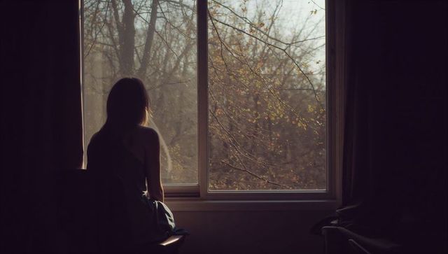 Woman Gazing Through Window at Bare Autumn Branches, Moody Silhouette and Quiet Solitude