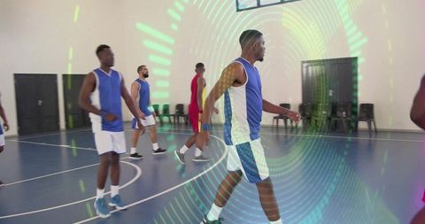 Male basketball players walking on indoor court with blue jerseys and green projection