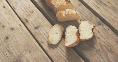 Partially sliced baguette resting on rustic wood plank with crumbs and warm natural light