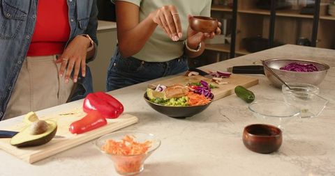 Diverse women preparing healthy salad on marble countertop with fresh vegetables