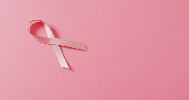 Pink ribbon symbolizing breast cancer awareness on solid pink background. Ideal for healthcare campaigns, awareness posters, charity event promotions, educational materials, and fundraising projects. The image conveys hope, support, and solidarity for those affected by breast cancer.