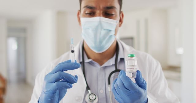 Hispanic male doctor preparing injection wearing face mask. medical professional making patient home visit during coronavirus covid 19 pandemic.